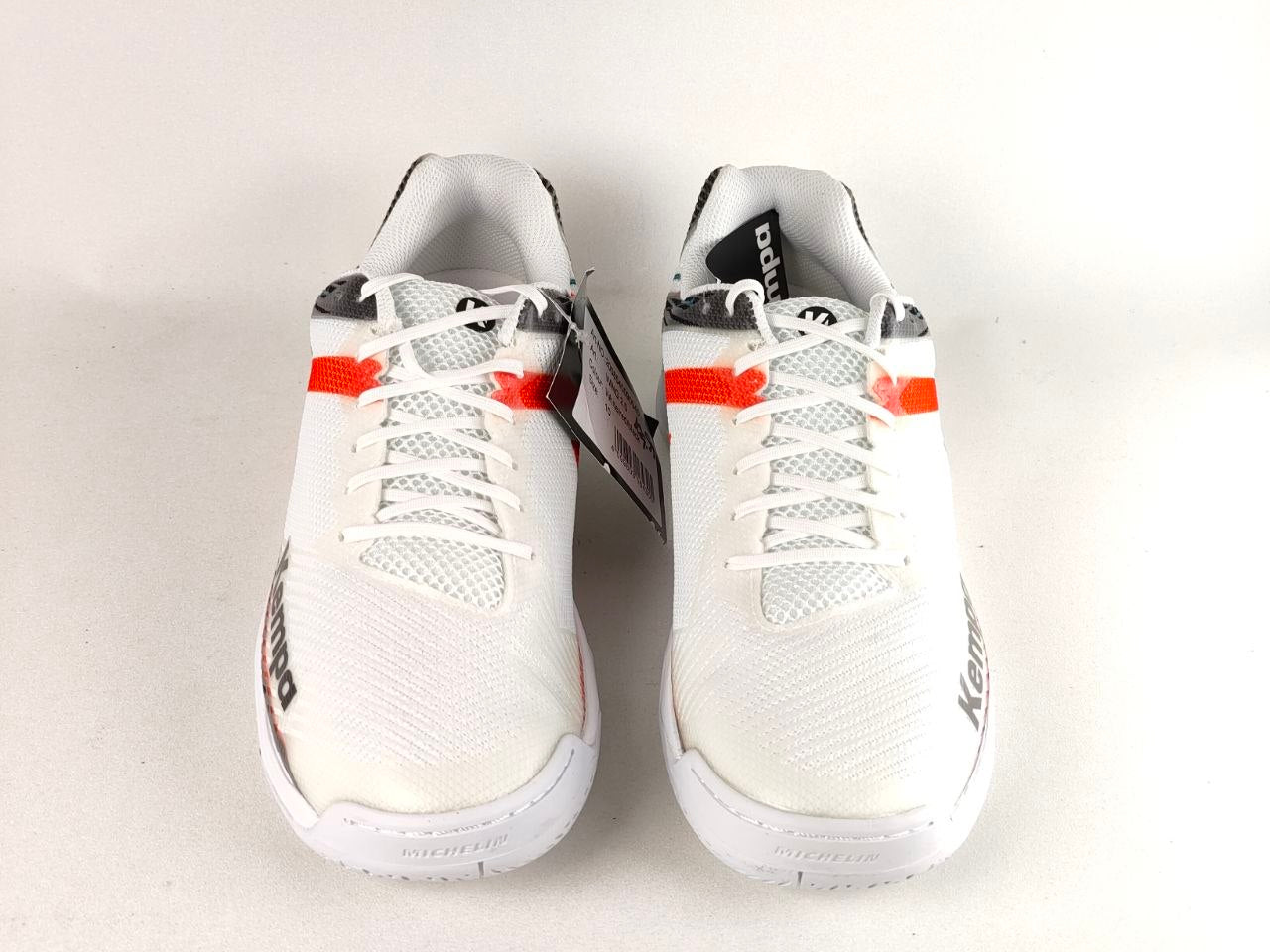 A pair of white K-Swiss athletic shoes with orange and black accents, shown from a top-down view on a light gray background.