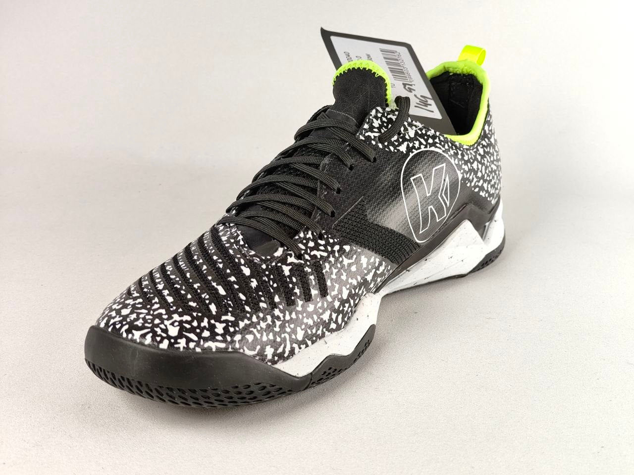 A New Balance low-top athletic shoe in black and white speckled knit, featuring a black laces, white midsole, and bright neon yellow-green accents on the collar and pull tab.