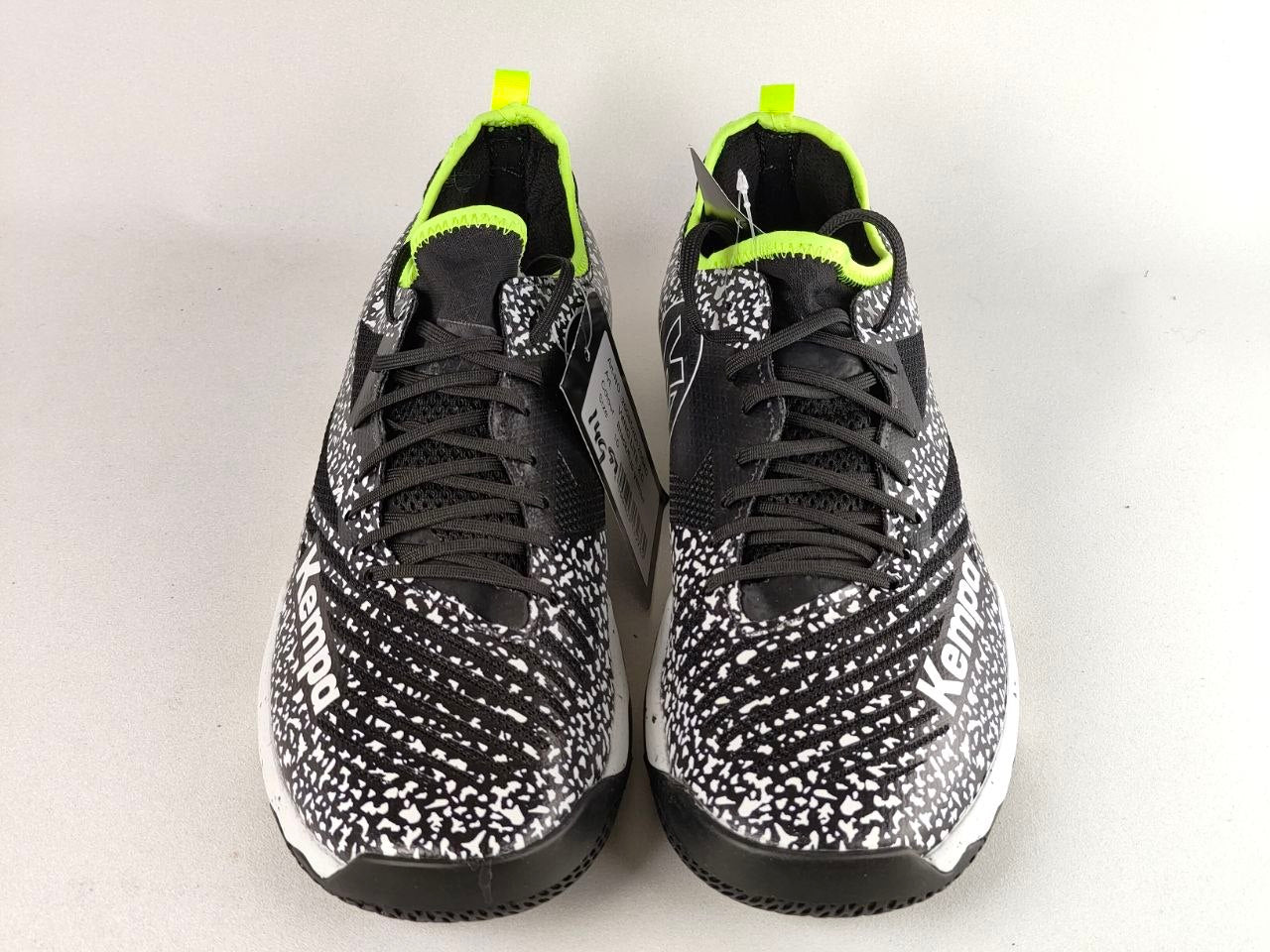 A pair of Puma sneakers with a black and white speckled pattern, black laces, and bright neon yellow accents on the collar and pull tabs, shown against a light gray background.