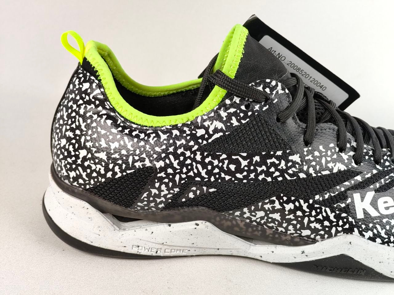 A close-up side view of a Reebok athletic shoe featuring a black and white speckled pattern, black mesh panels, a bright neon yellow-green collar lining, and a white and black textured midsole.