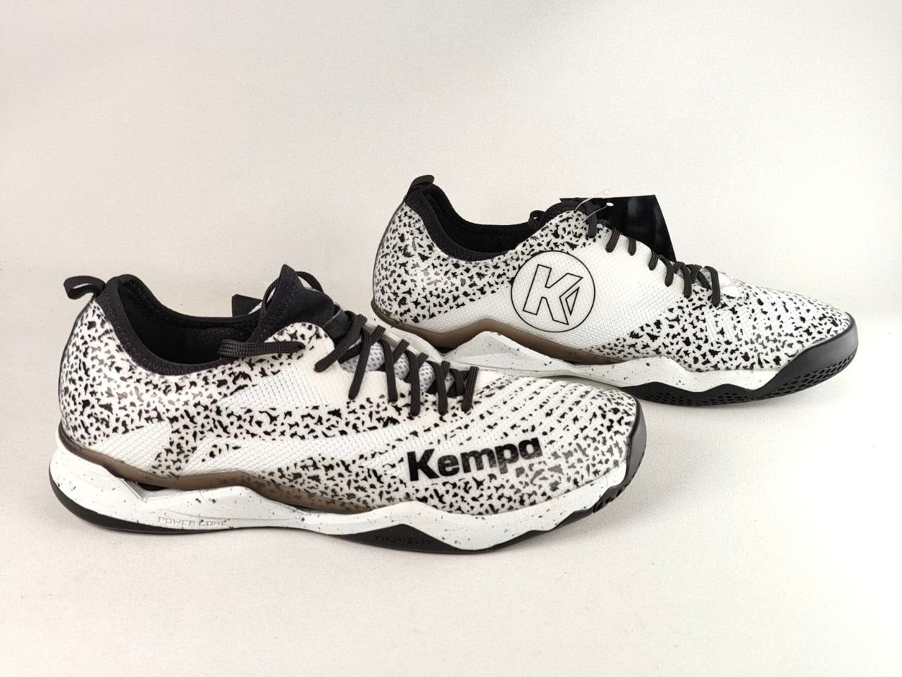 A pair of Kempa brand athletic sneakers with a white and black speckled pattern, black laces, and a black sole, displayed on a light gray background.