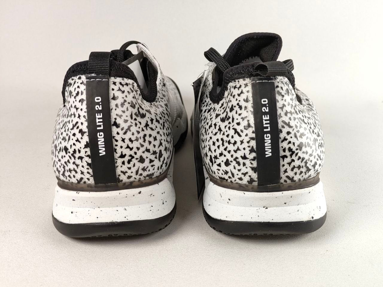 A pair of low-top sneakers shown from the back, featuring a black and white speckled pattern on the upper, a black vertical strap with 'WING LITE 2.0' text, and a white and black speckled midsole.