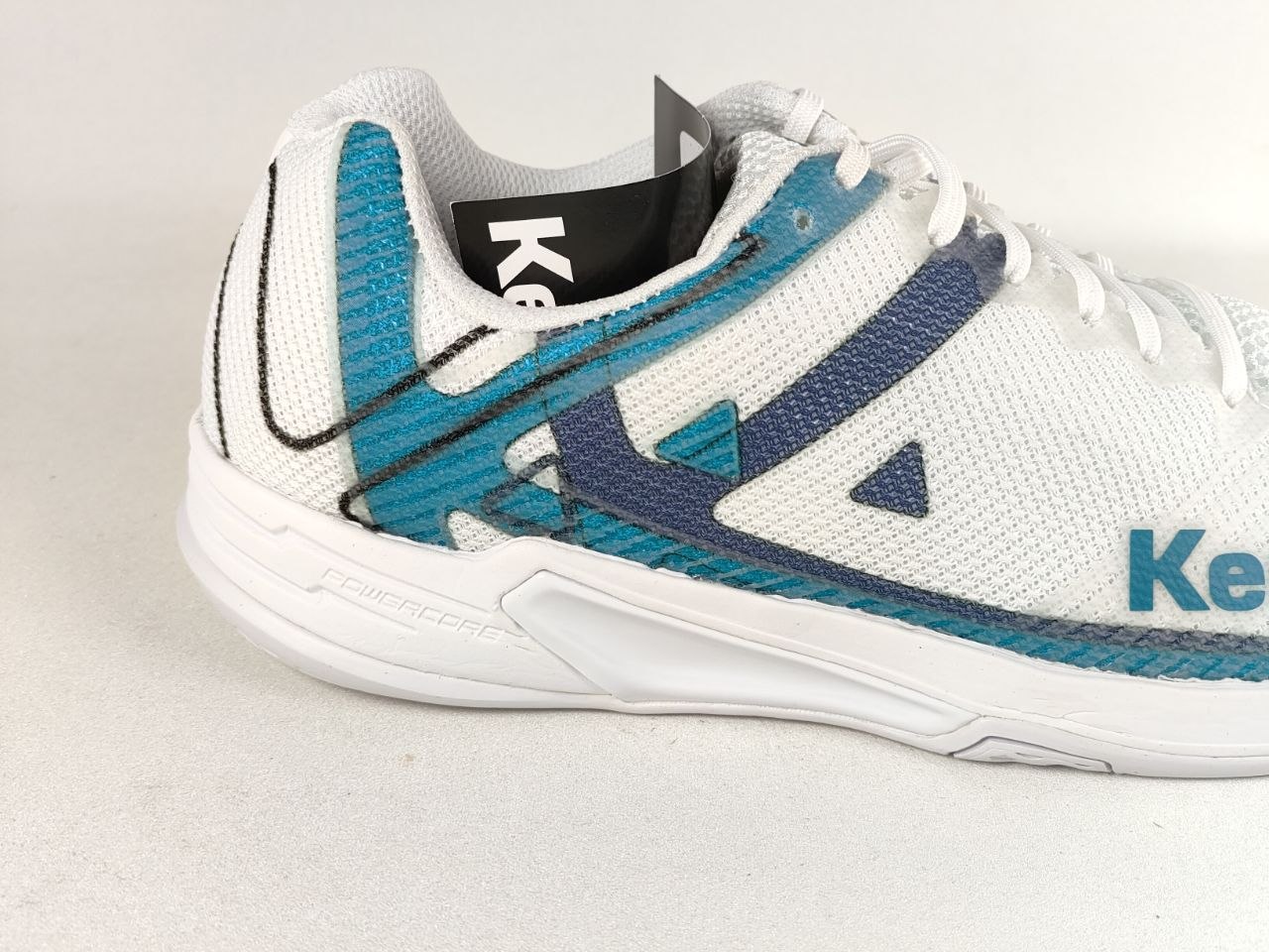A close-up side view of a white athletic shoe with teal and navy blue accents, featuring the Keen logo on the side and heel.