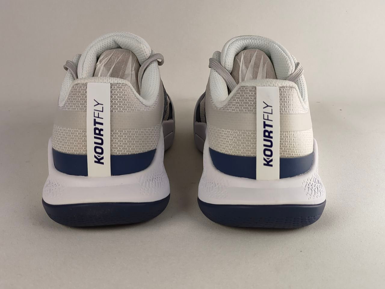 A pair of Kourt Fly basketball shoes shown from the back, featuring a white and light gray knit upper with navy blue accents and a white heel tab with 'KOURTFLY' printed vertically.