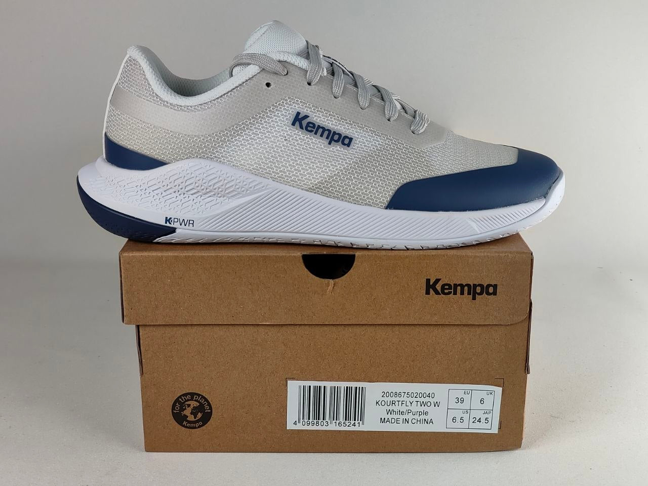 A light gray and navy blue Kempa running shoe resting on top of its brown cardboard packaging box, set against a plain light gray background.
