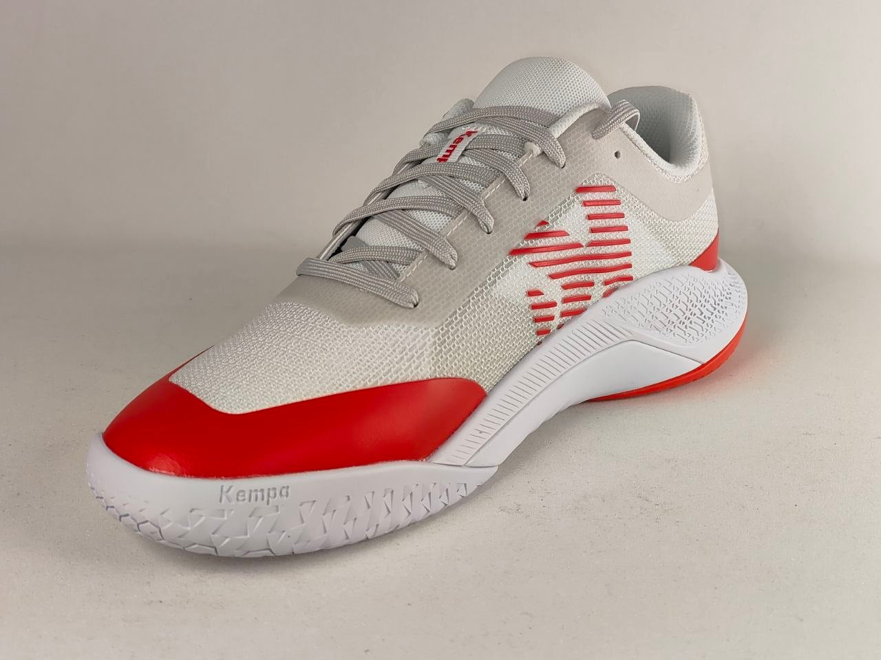 A Kappa athletic shoe in white and red, featuring a textured knit upper, gray laces, and a red toe cap, shown against a neutral light gray background.