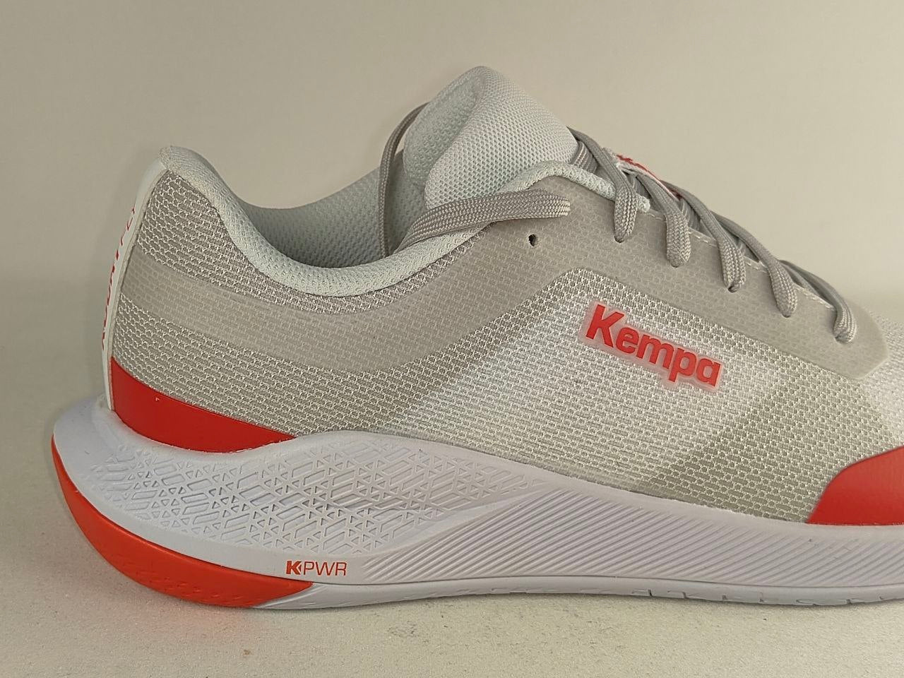 A light gray and white running shoe with bright red accents, featuring the Kempa logo on the side and a white sole with red KPWR branding.