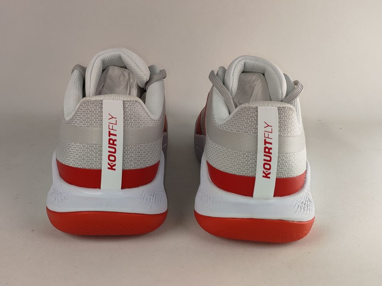 A pair of Kourt Fly basketball shoes shown from the back, featuring a light gray mesh upper, white midsoles, and bright red outsoles.