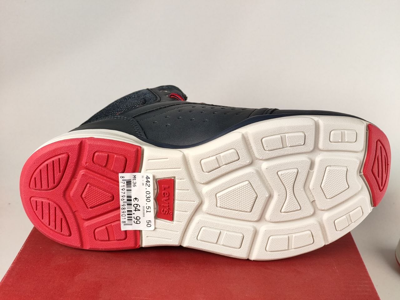 The outsole of a low-top sneaker, showing a dark navy blue upper, a white textured tread pattern, and bright pinkish-red rubber outsole sections on the heel and toe, resting on a red surface against a light gray background.
