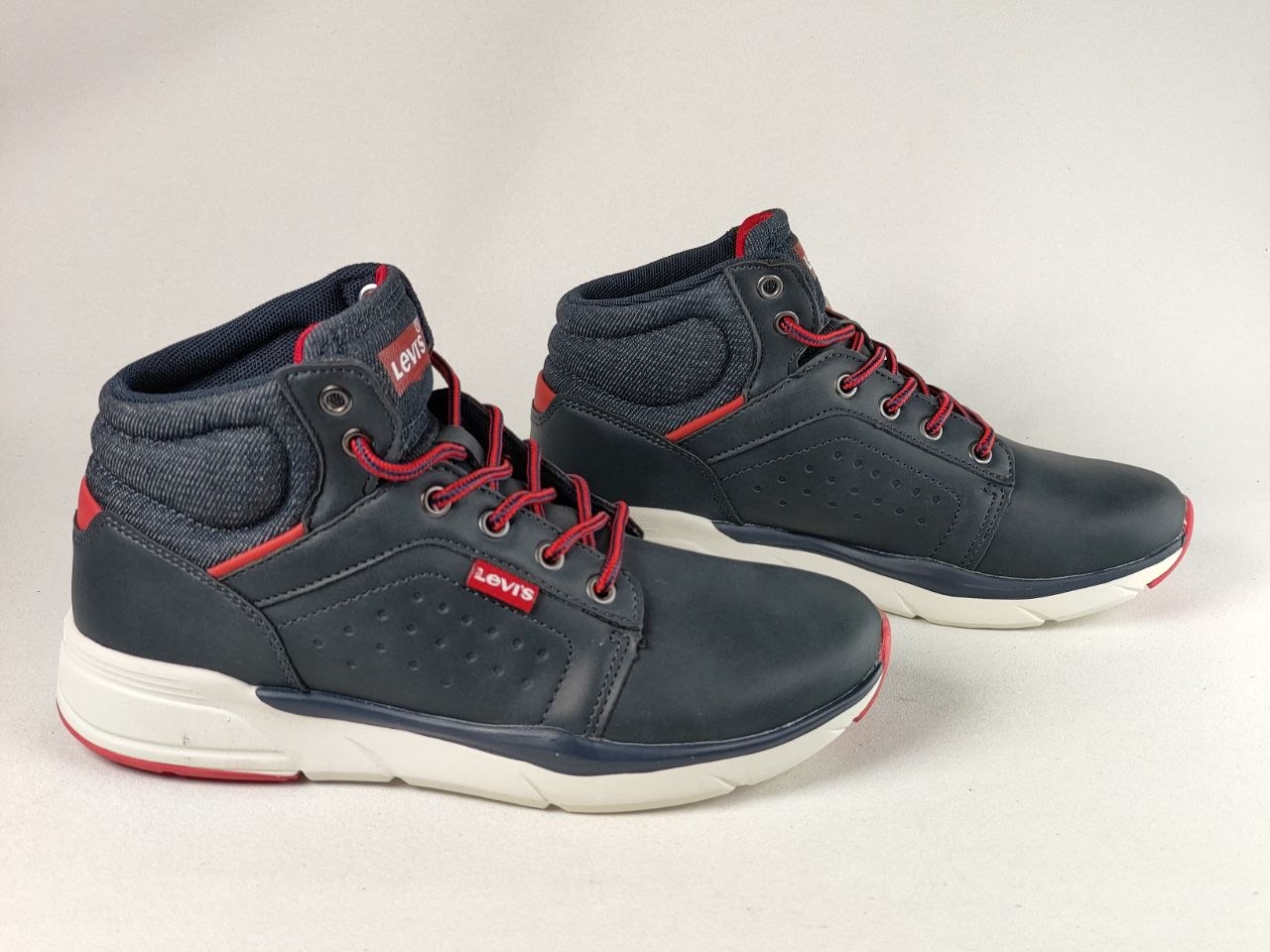 A pair of Levi's mid-top sneakers in navy blue with red laces, red accents, and a white sole, photographed on a light gray background.