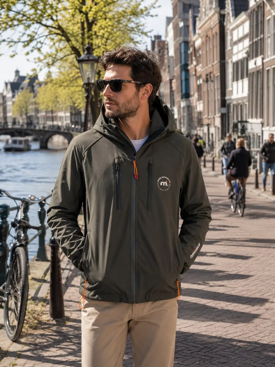 Man wearing a dark jacket with a logo standing on a street in an urban setting.