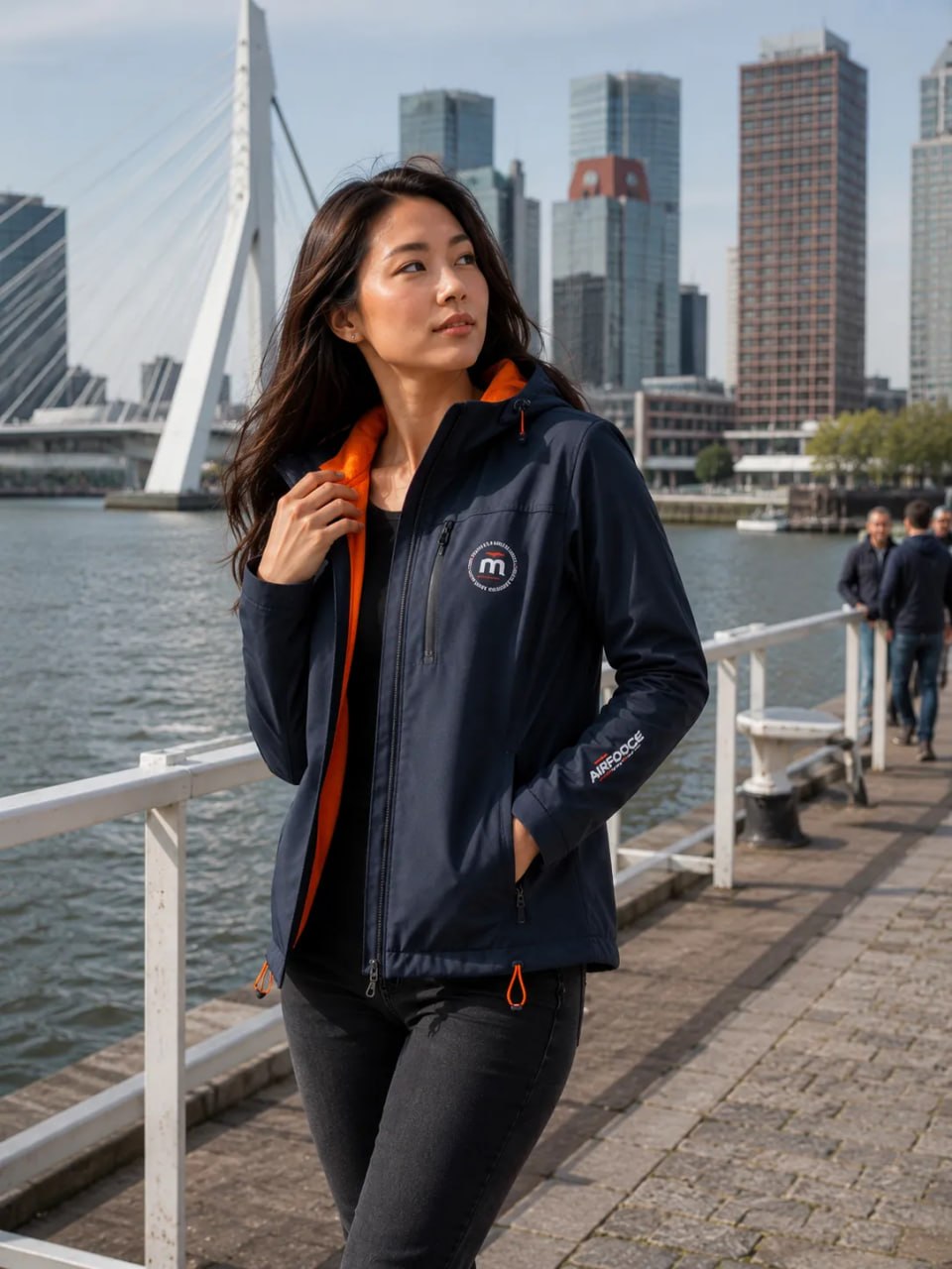 Woman wearing a navy jacket with orange accents by a waterfront with city skyline in the background