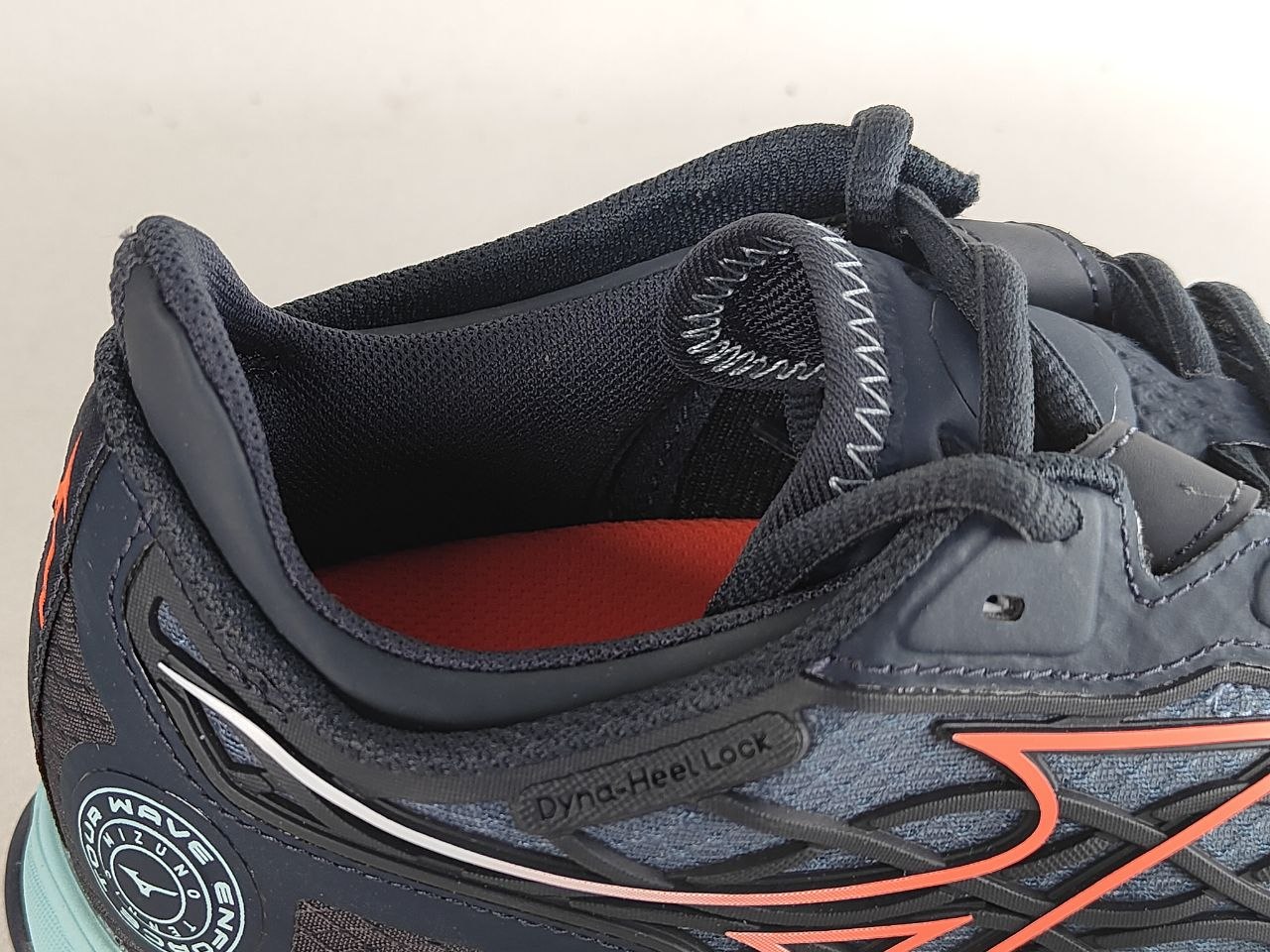 Close-up of a dark gray and black running shoe with orange accents, showing the heel area, laces, and interior lining.