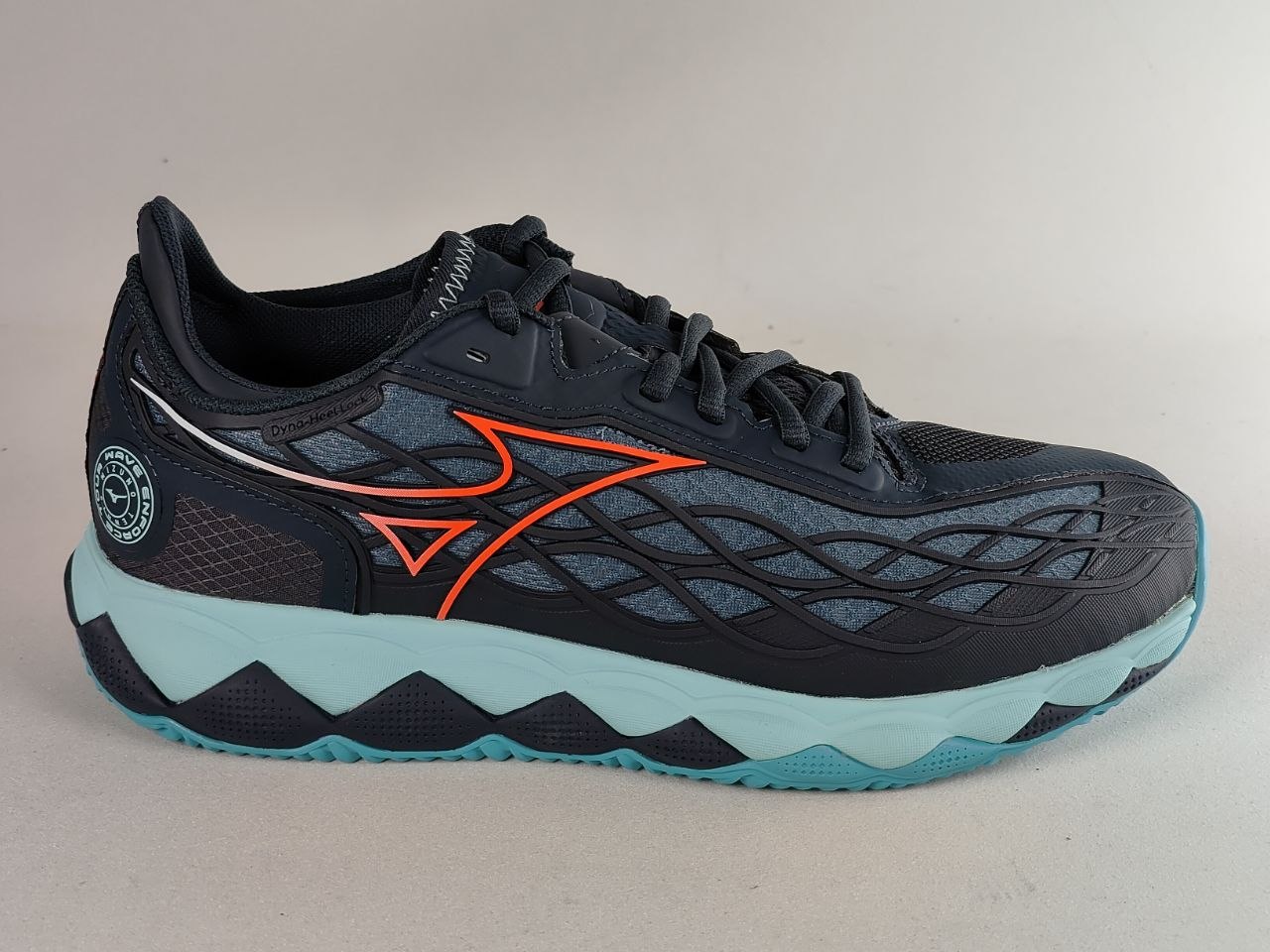 A Mizuno running shoe in black and dark gray with a bright orange logo, a light blue midsole, and a turquoise outsole, shown against a neutral light gray background.