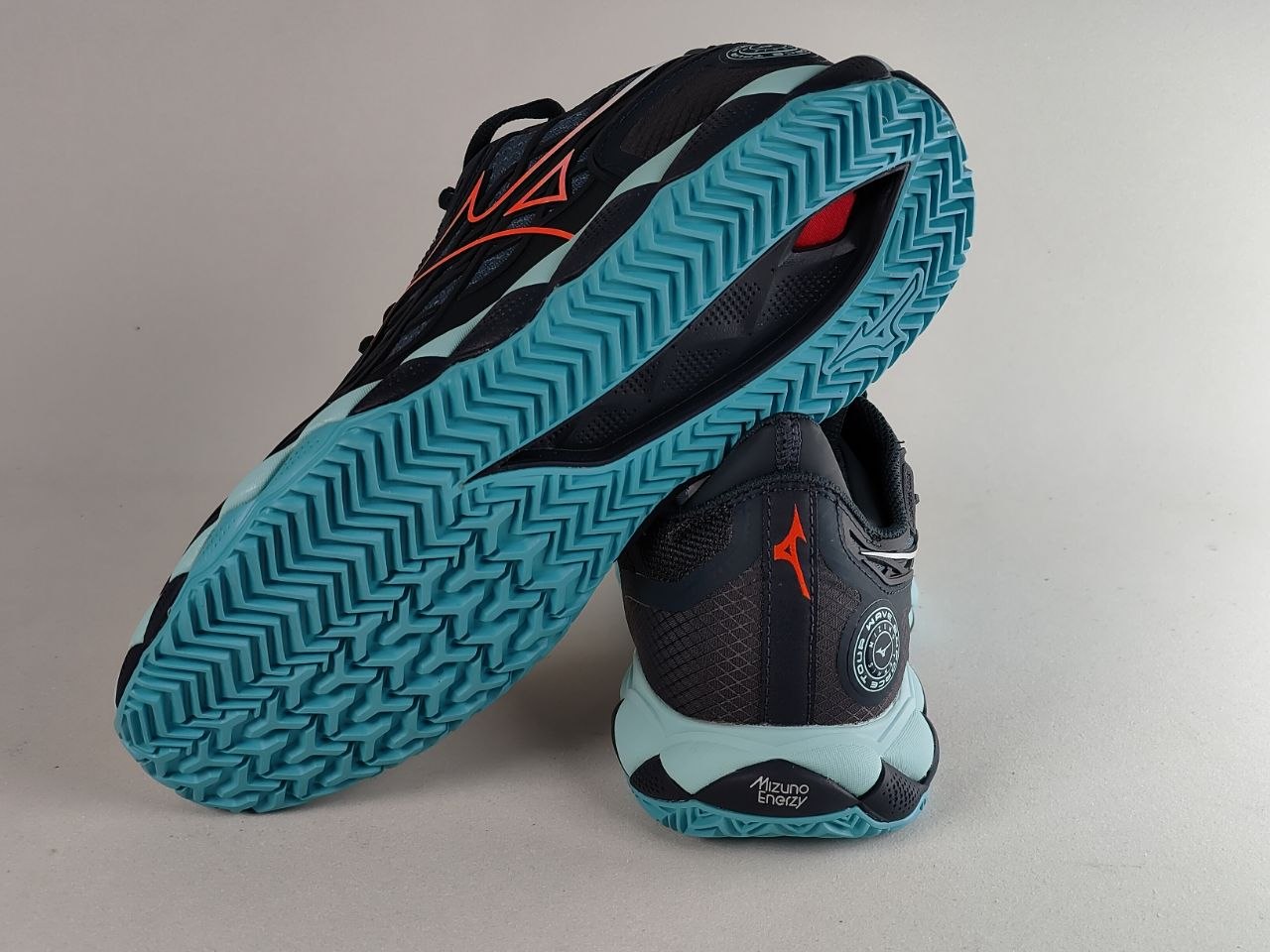 A pair of athletic sneakers shown on a neutral light gray background, with one shoe standing upright to display the side profile and the other lying on its side to show the textured blue and black outsole.