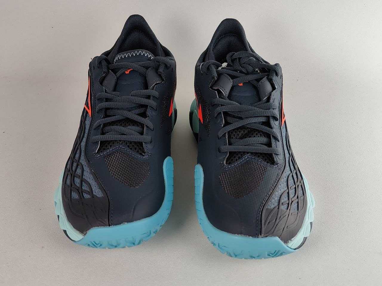 A pair of Nike running shoes in dark navy blue with bright orange accents and light blue soles, shown from the front on a neutral light gray background.