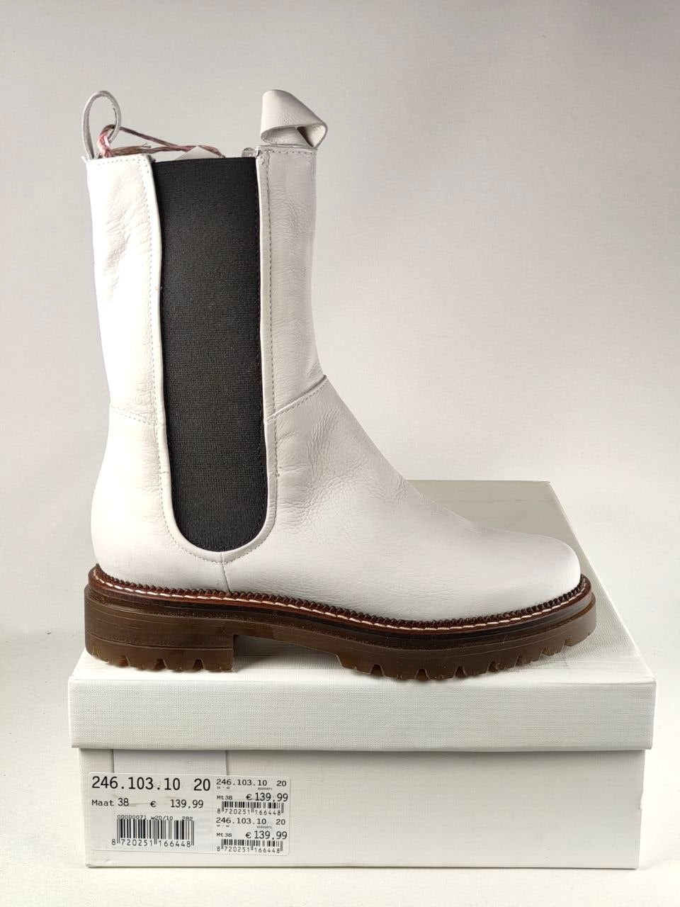A white leather Chelsea boot with a black elastic side panel and a brown lug sole, displayed on top of its white shoebox against a neutral light gray background.