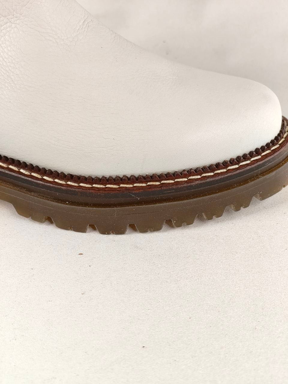 Close-up of a white leather boot showing the toe, welt, and brown lug sole against a light neutral background.