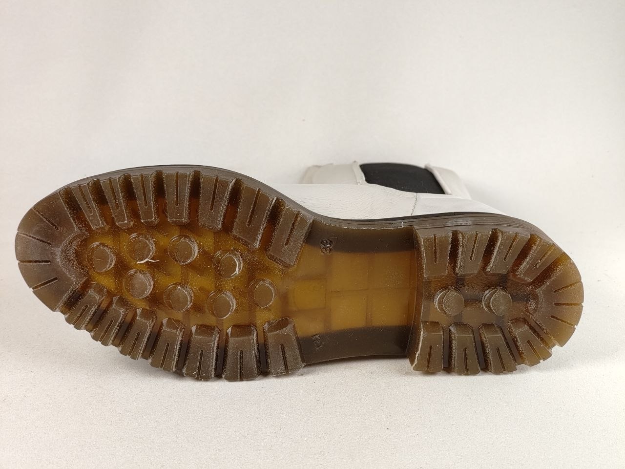 The outsole of a white boot with a brown lug tread, photographed against a plain off-white background.