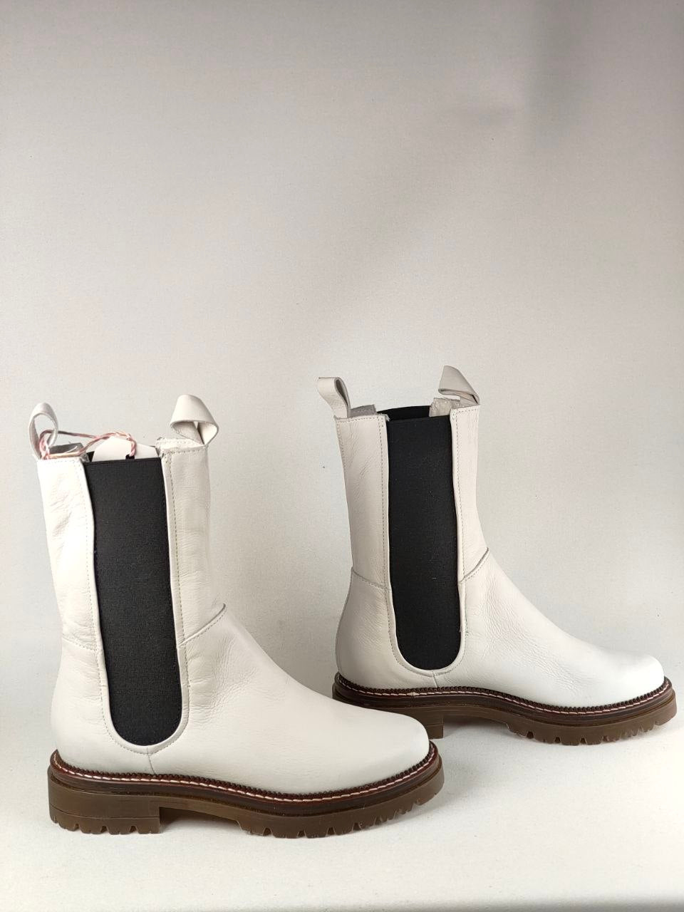 A pair of white leather Chelsea-style boots with black elastic side panels and brown soles, photographed against a plain light gray background.