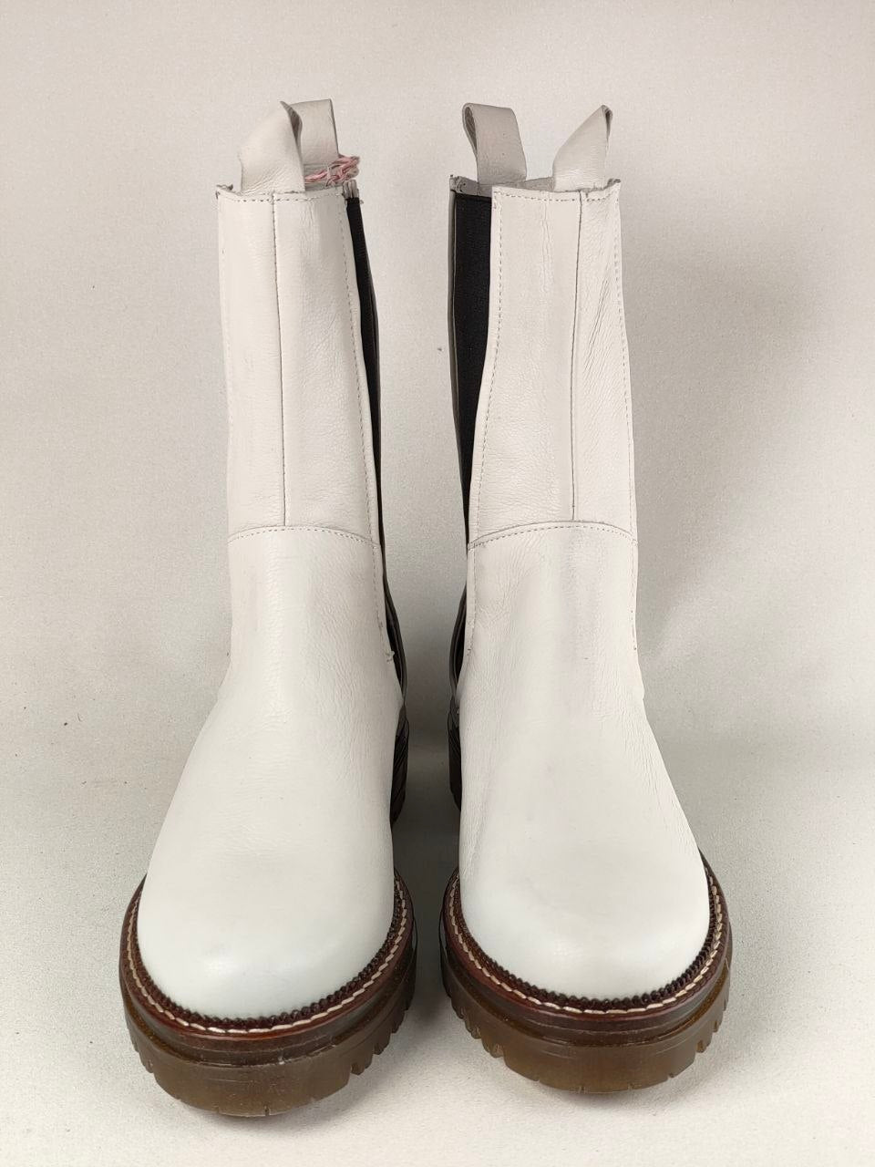 A pair of white leather Chelsea boots with brown platform soles, shown from the front against a light gray background.