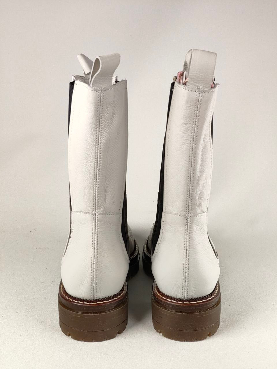 A pair of white leather ankle boots with brown platform soles and black side panels, shown from the back against a light gray background.