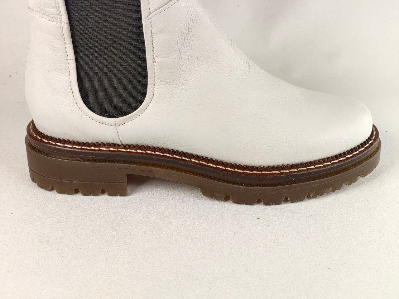 A white leather Chelsea boot shown in a side profile view, featuring a dark brown lug sole and contrast stitching.