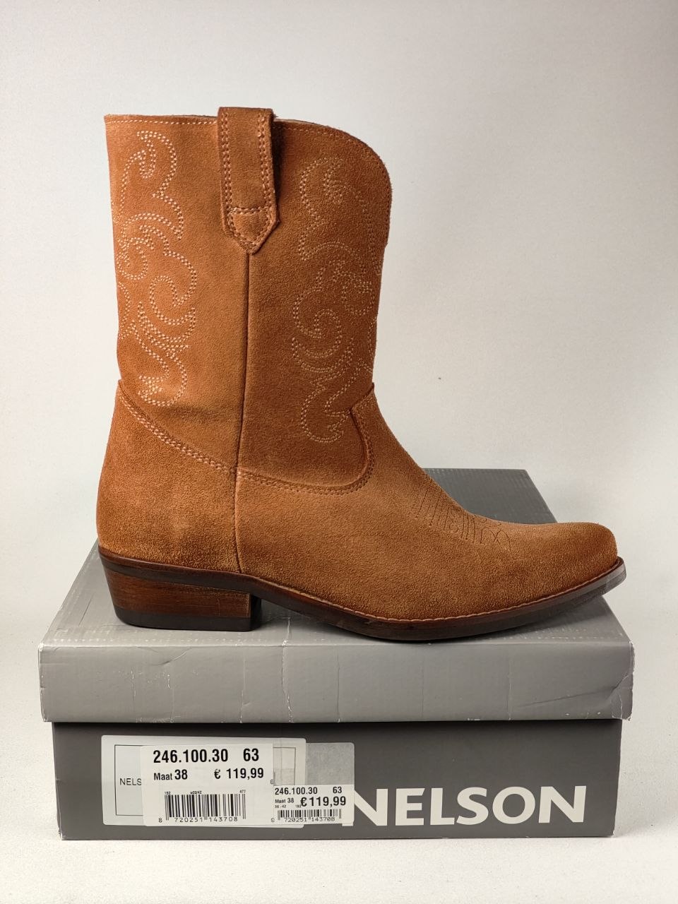 A tan suede western boot with embossed scrollwork, displayed on top of its gray Nelson shoebox against a light gray background.