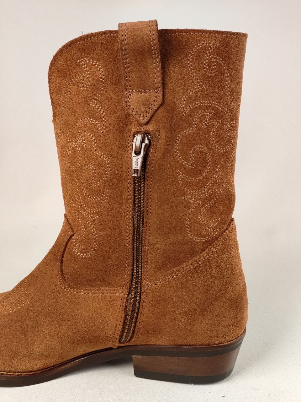 A brown suede western-style boot with a side zipper, decorative stitched embroidery, and a low stacked heel, shown against a plain light background.