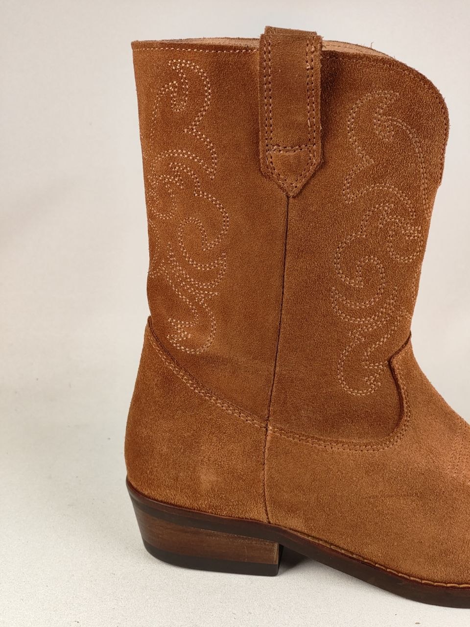 A close-up side view of a brown suede western boot with decorative stitching on the shaft, set against a plain light background.