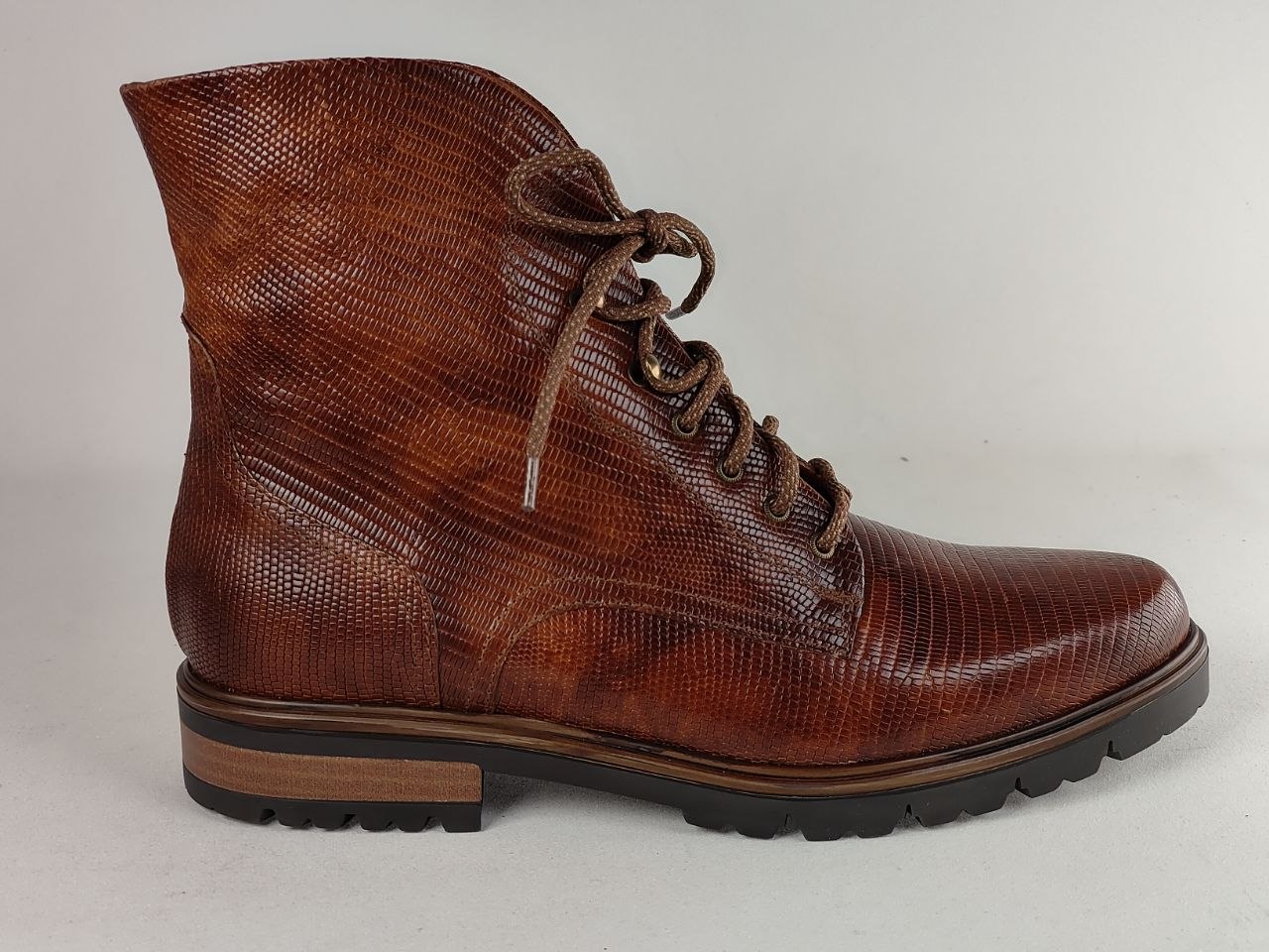 A single brown textured lace-up ankle boot with a snakeskin pattern, brown laces, and a stacked sole, photographed against a neutral light gray background.