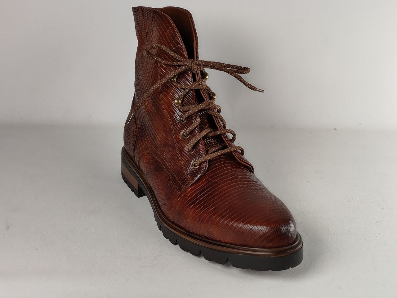 A single brown leather lace-up boot with a textured, reptile-like embossed pattern, photographed on a neutral light gray background.