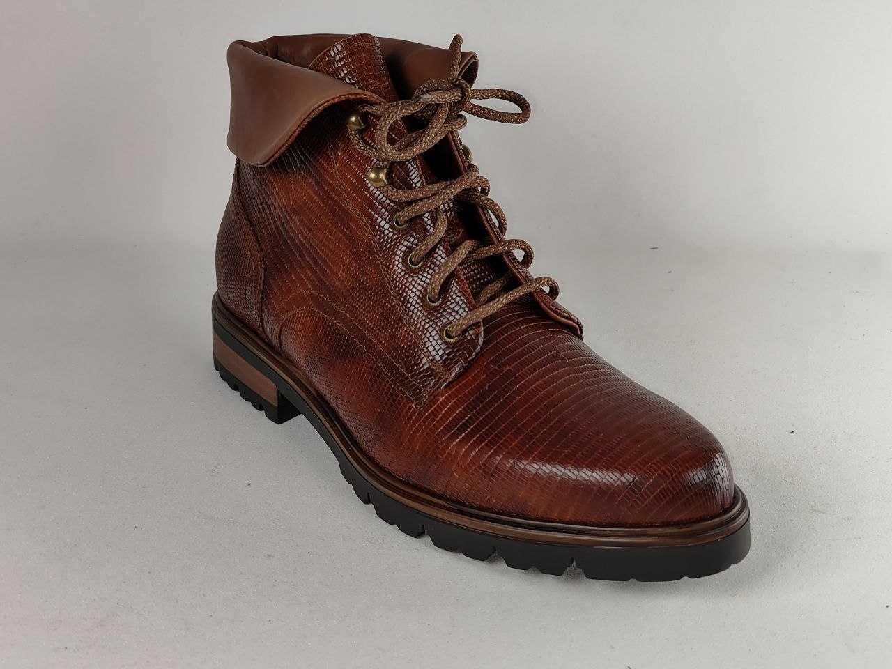 A single brown textured leather lace-up boot with a rugged black sole, photographed on a neutral light gray background.