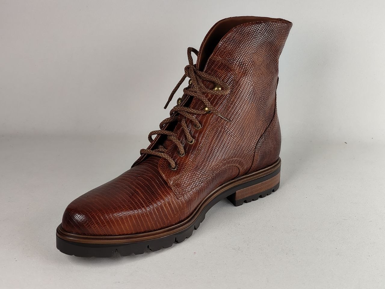 A brown textured leather lace-up boot with a reptile-like embossed pattern, dark sole, and brown laces, photographed on a light gray background.
