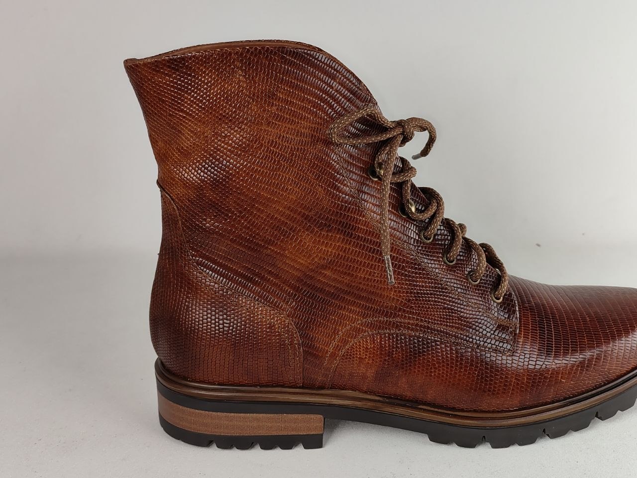 A brown textured leather lace-up ankle boot with a reptile-like embossed pattern, set against a plain light gray background.