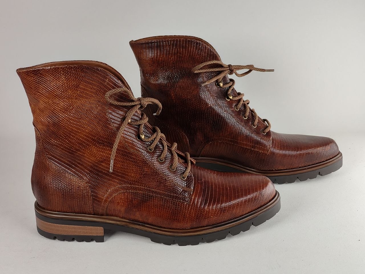A pair of brown textured leather lace-up ankle boots with a glossy finish, displayed on a light gray background.