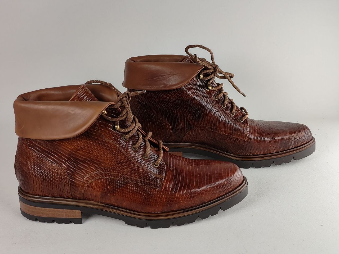 A pair of men's brown leather lace-up boots with a textured reptile-patterned upper and smooth leather collar, shown on a light gray background.