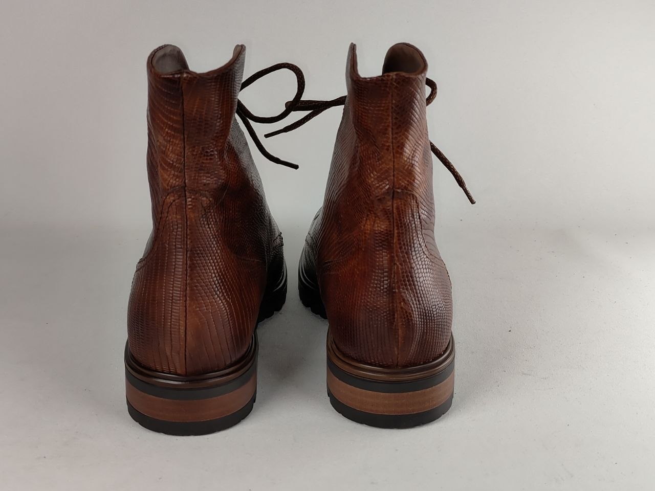 A pair of brown textured leather lace-up ankle boots shown from the back against a light gray background.