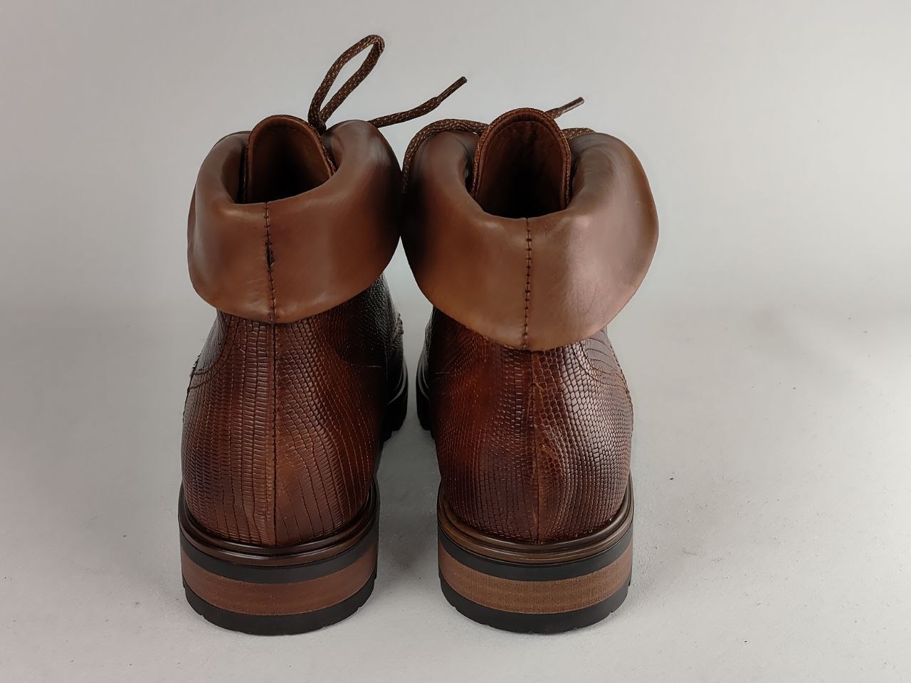 A pair of brown leather ankle boots with textured sides, thick stacked brown soles, and elasticized cuffs, shown from the back on a light gray background.