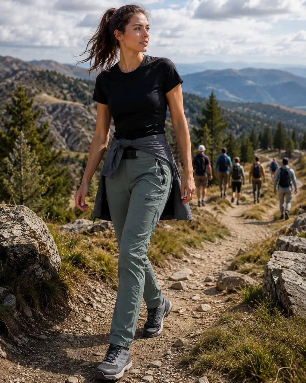 woman hiking in black T-shirt and a green ONeill Hybrid Soft shell Outdoor Pants with mountain backgroung