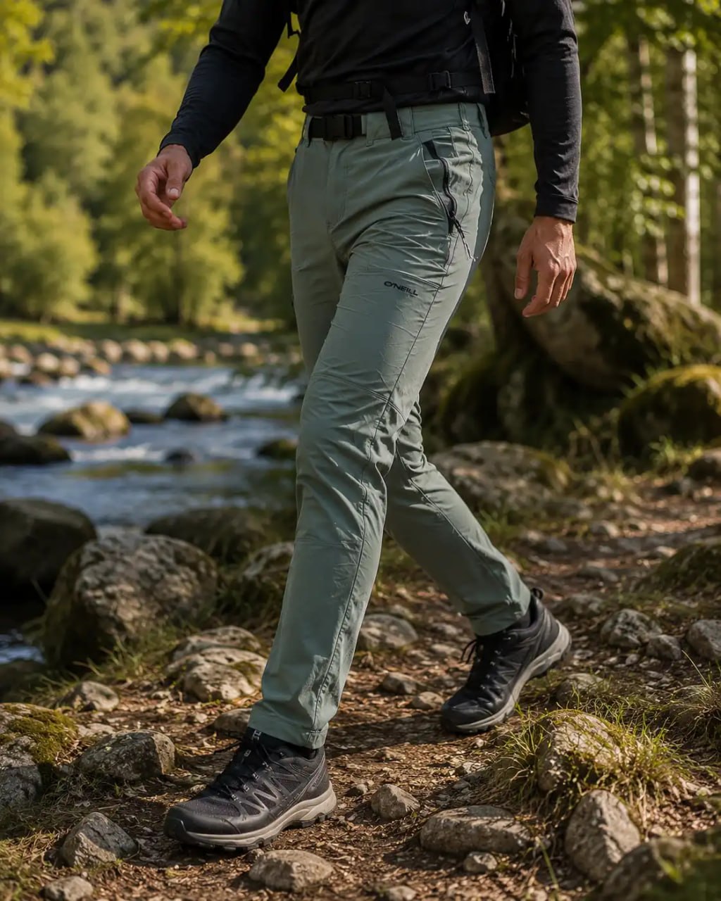 Person wearing green hiking ONeill Hybrid Soft shell Outdoor Pants and shoes walking on a rocky trail with a forest background