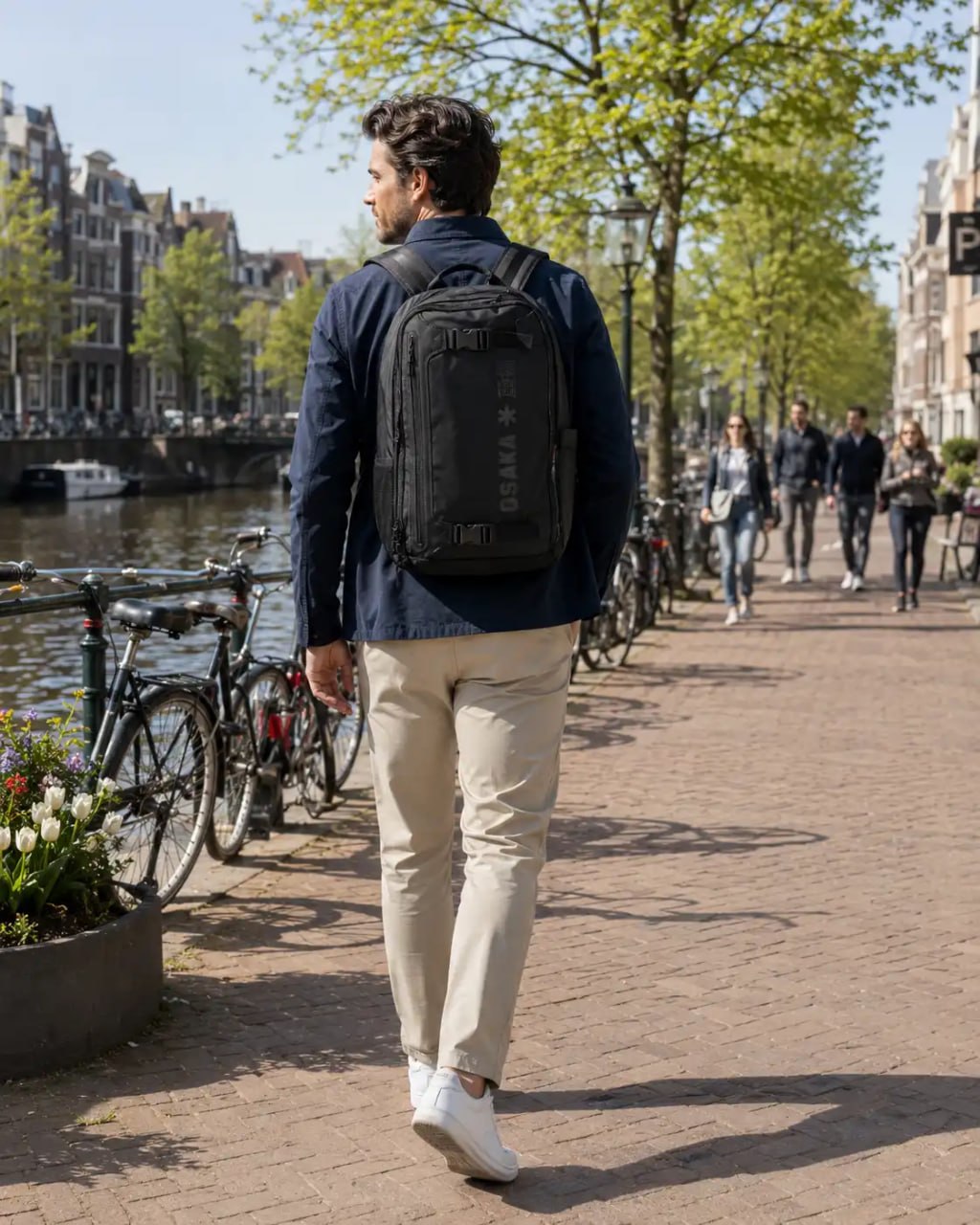 Man walking along a canal in a European city with a backpack