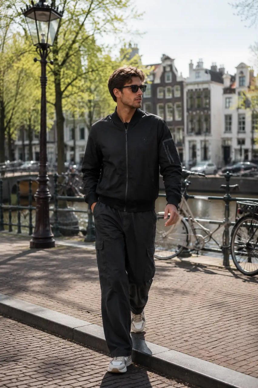 Man in black jacket and pants walking on a street with buildings and bicycles in the background