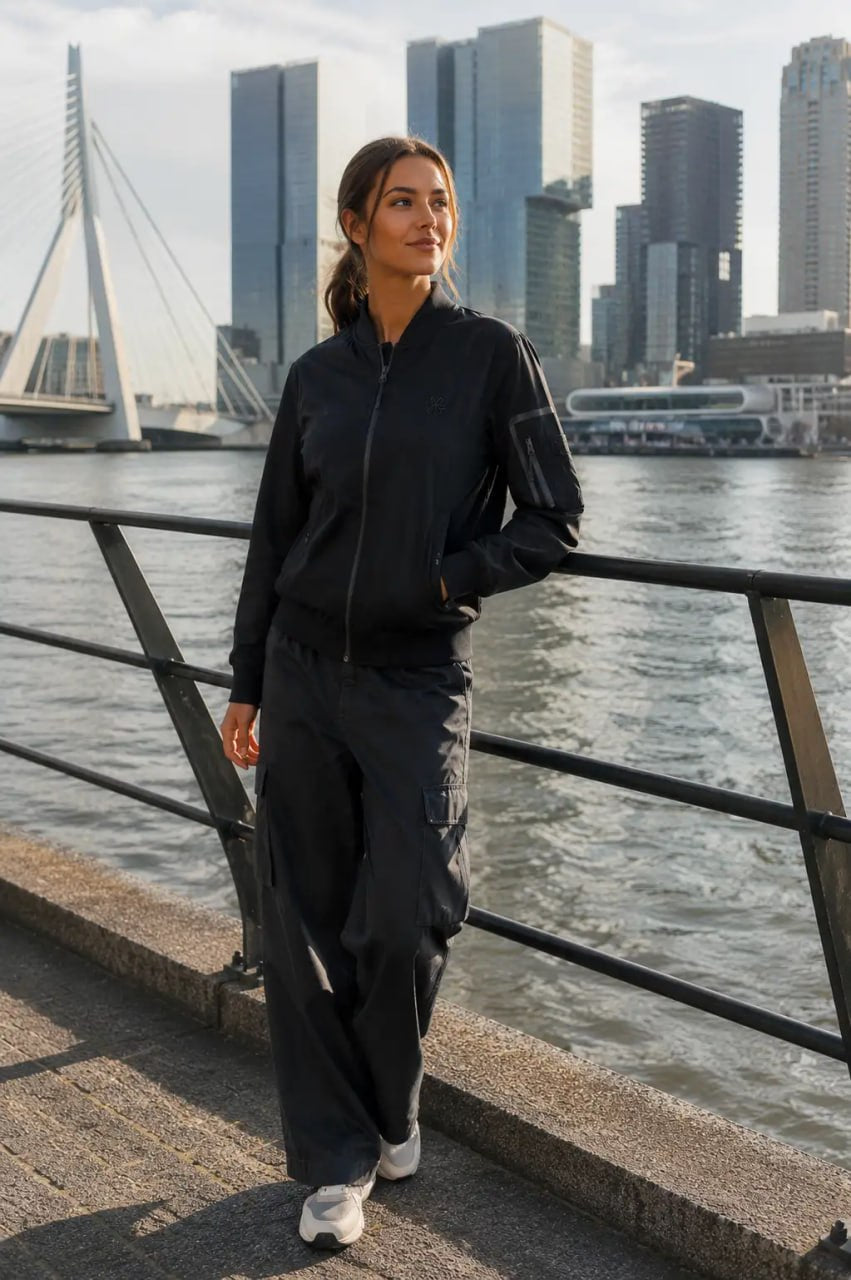 Woman in black outfit standing by a waterfront with city skyline in the background