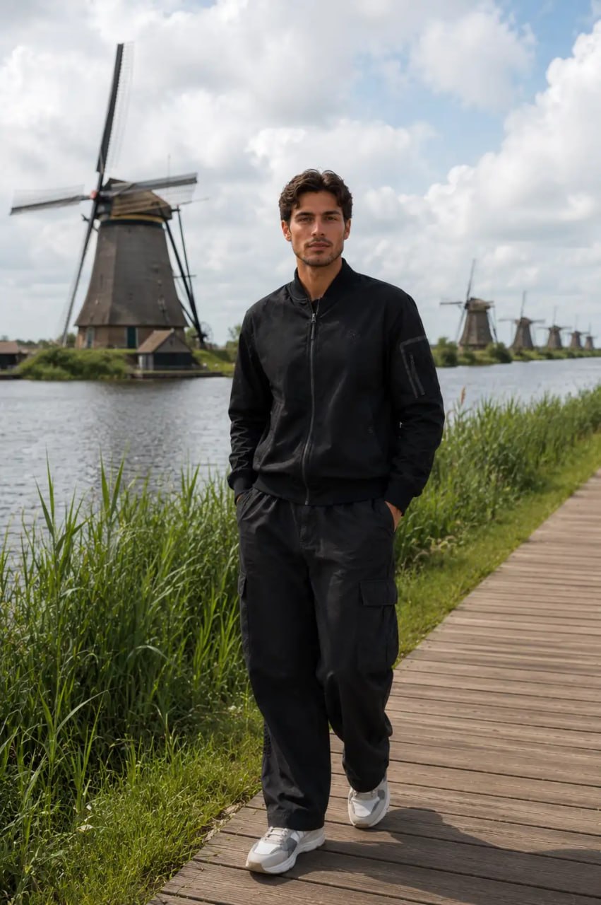 Man standing on a wooden path by a body of water with windmills in the background