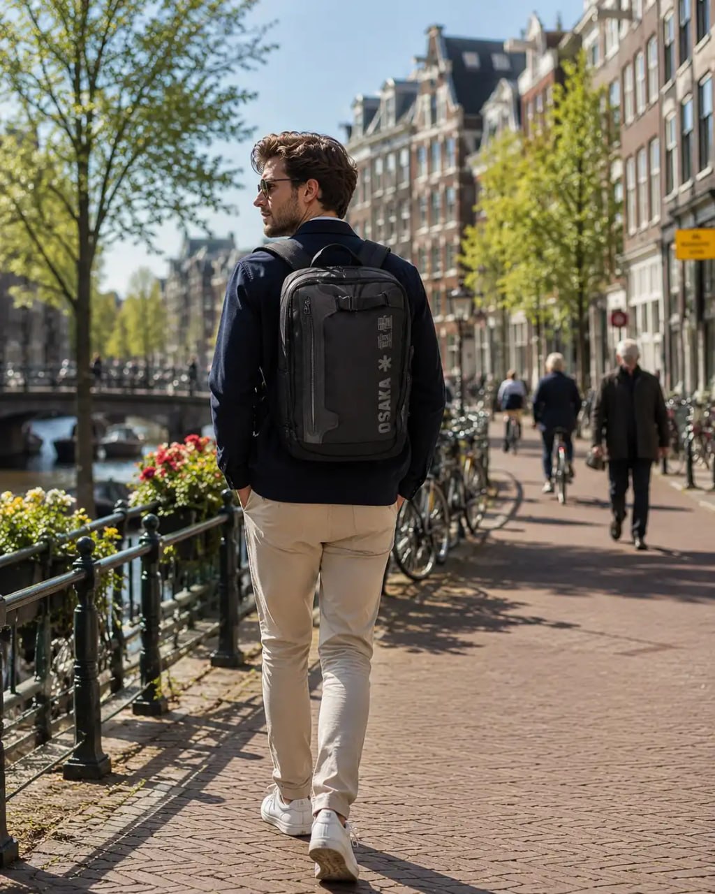Man walking with a black backpack on a city street with buildings and bicycles in the background.