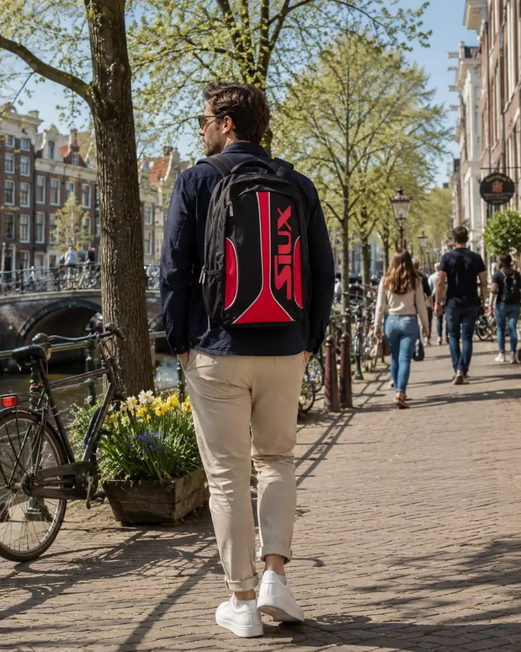 Man walking on a street in an urban setting with a red and black backpack.
