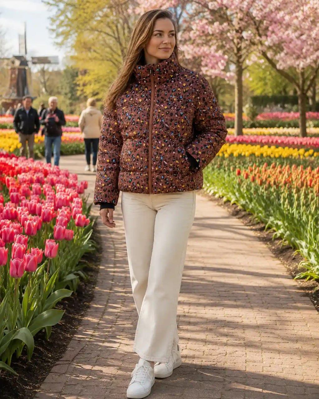 Woman walking through a tulip garden wearing a colorful patterned Stronger heat short jacket and white pants.