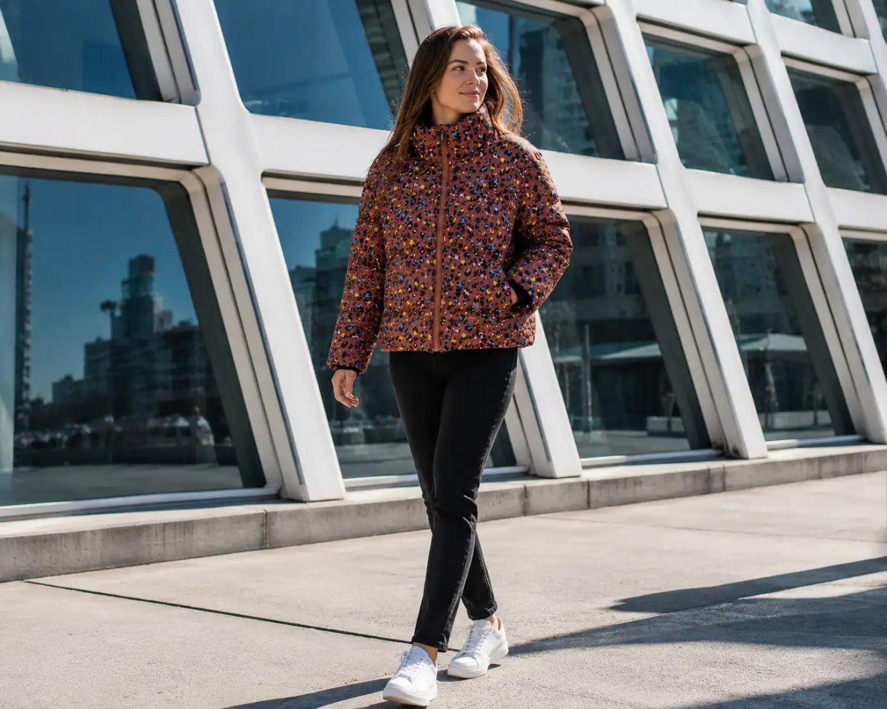 Woman wearing a colorful patterned Stronger heat short jacket standing in front of a modern building with large windows.